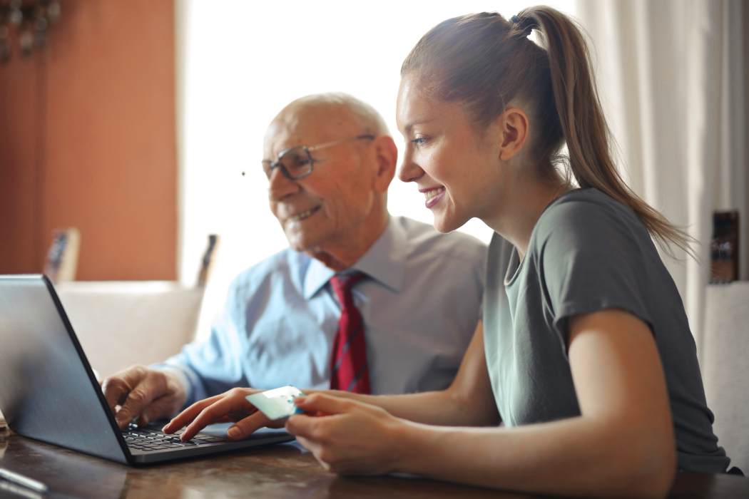 woman helping a man make an online payment at a laptop