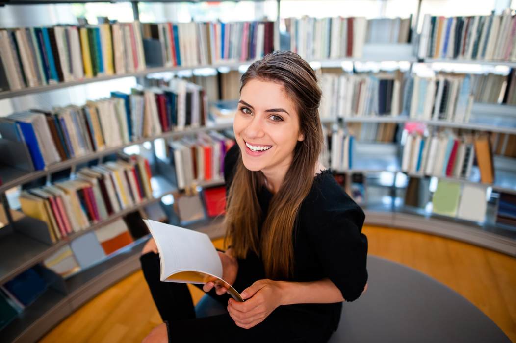 Smiling woman holding a book in front of shelves of books in a library