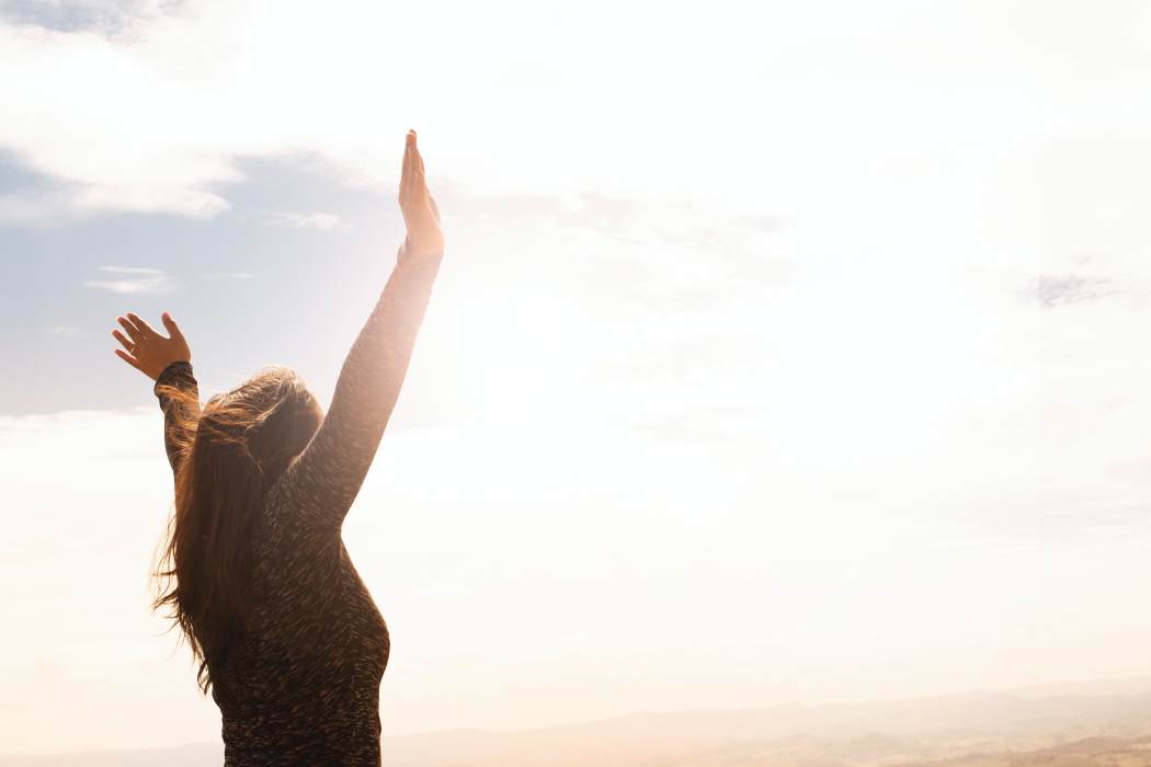 woman raising both hands into the air against a sunshine background