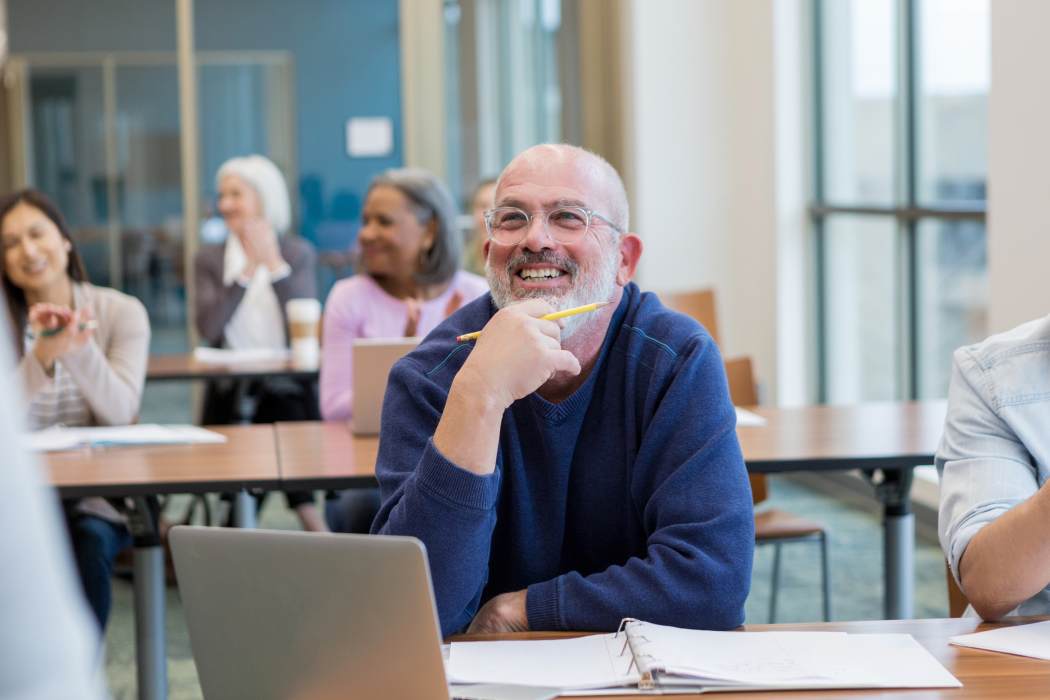 Man sitting at the front of an adult learning class with fellow learners in the background.