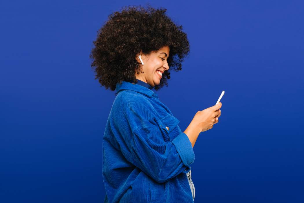 Smiling woman with curly hair looking down at her mobile phone in her hands