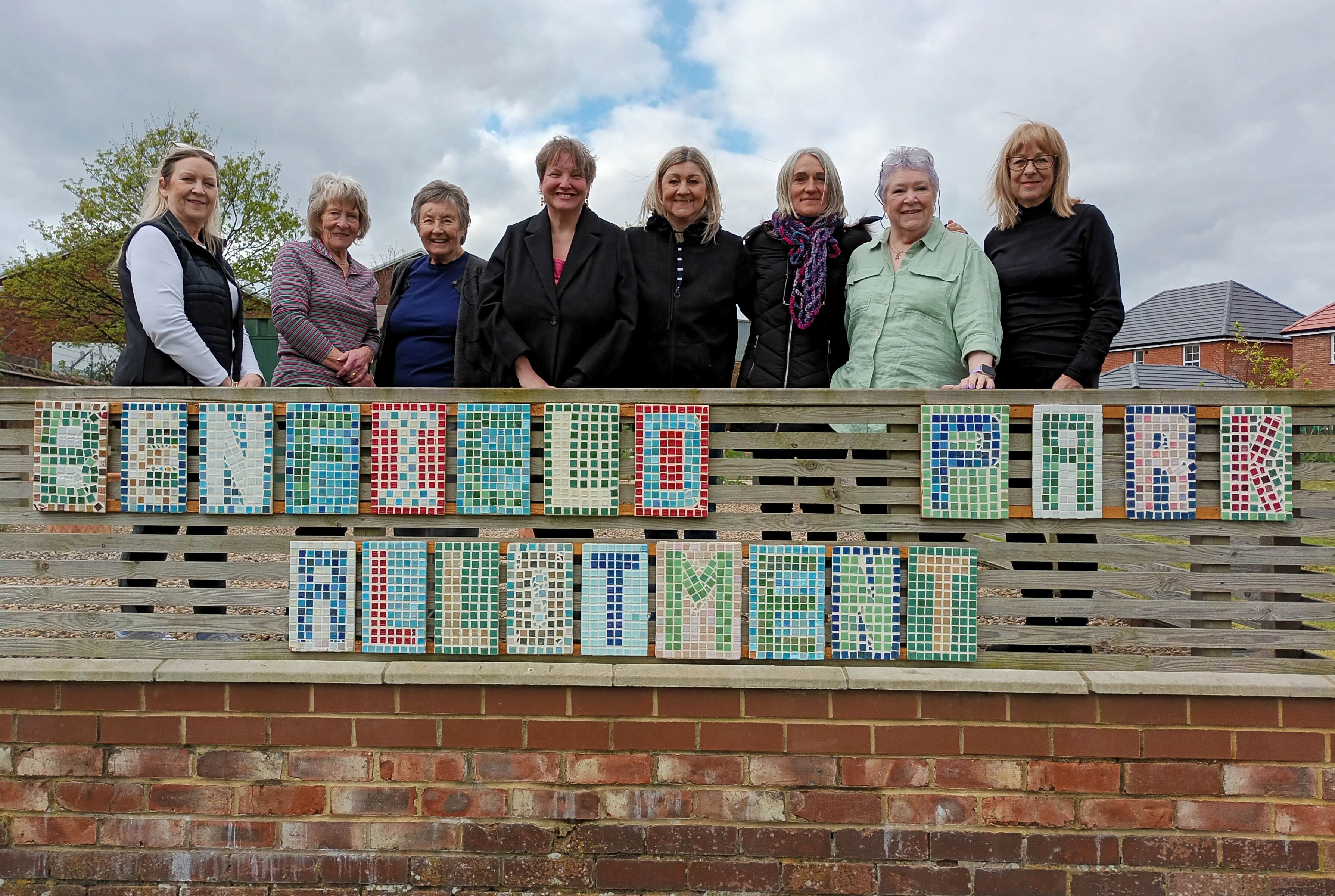 Group of learners standing above their mosaic tile creations in allotment.